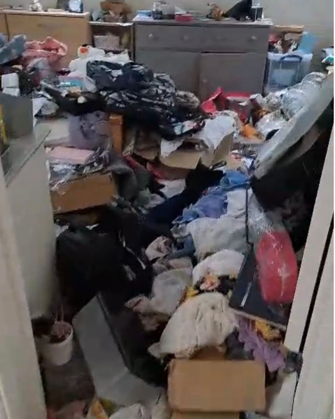 Messy loft room filled with cardboard boxes, bags, and household clutter in front of a bookshelf beneath a skylight window