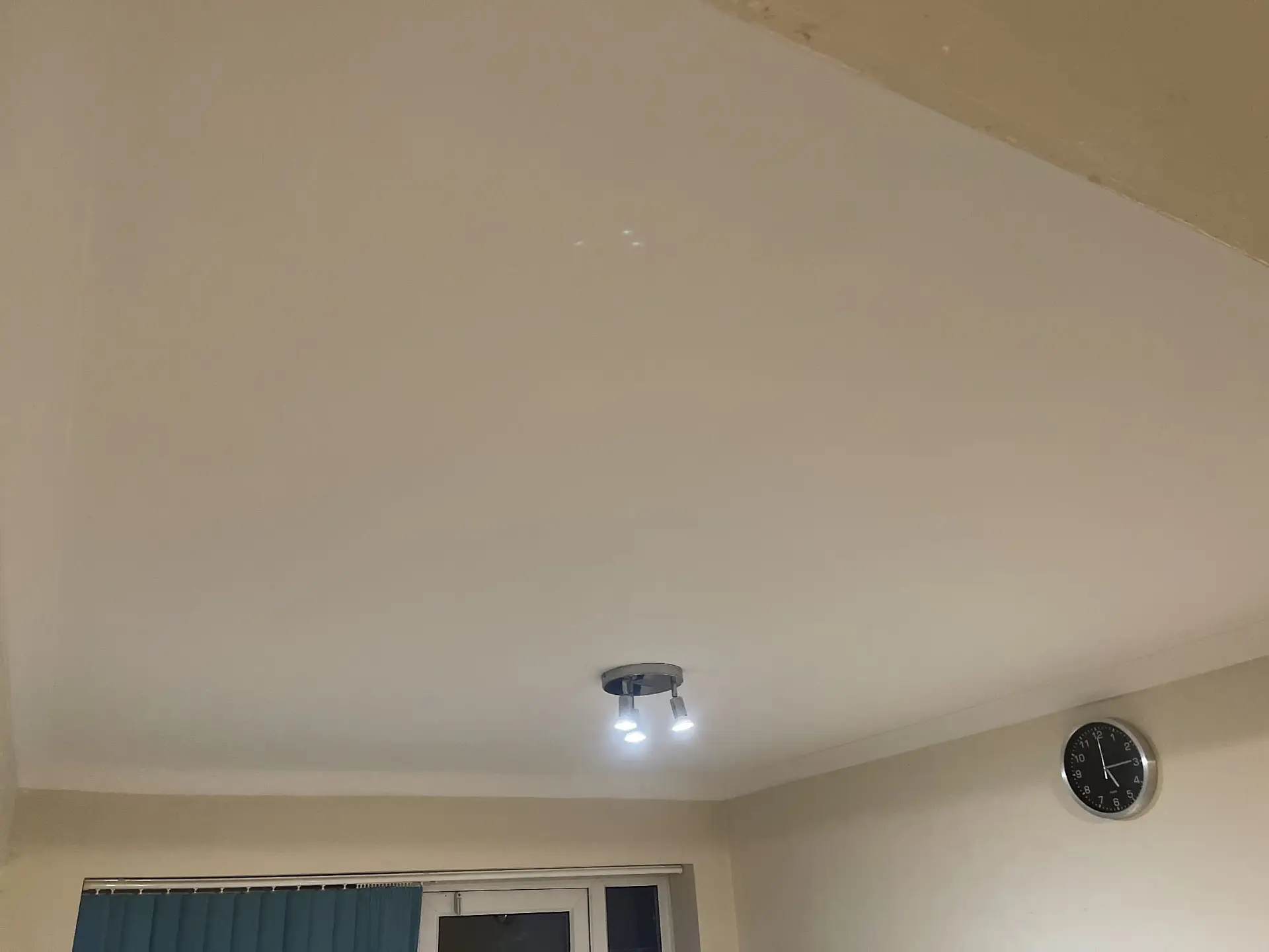 Smooth white painted ceiling with two-light spotlight fitting above a room with patio doors and wall clock.