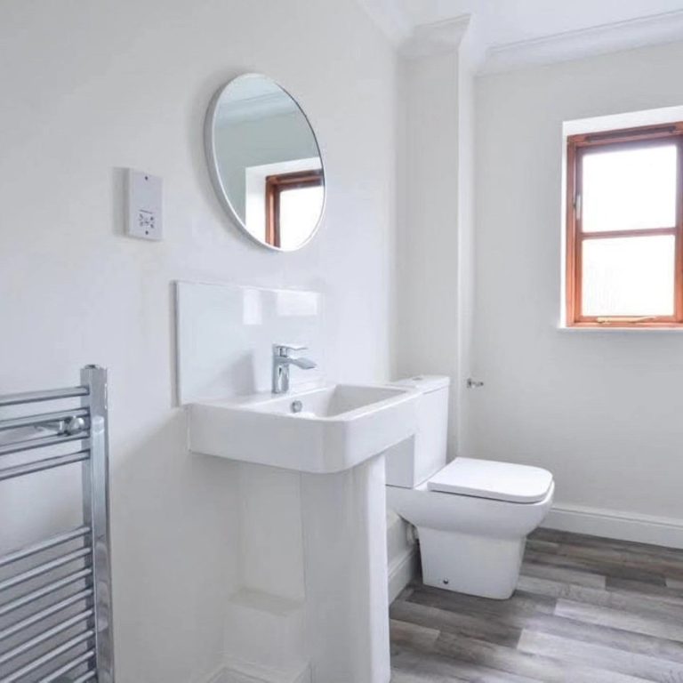 Modern bathroom with a wall-mounted sink, toilet, and a round mirror above the sink.