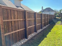 A wooden fence extends alongside a grassy yard under a clear blue sky.