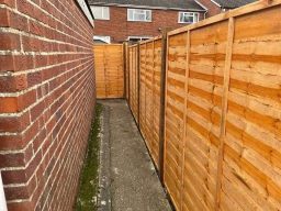 Narrow pathway between wooden fences leading to a gate.