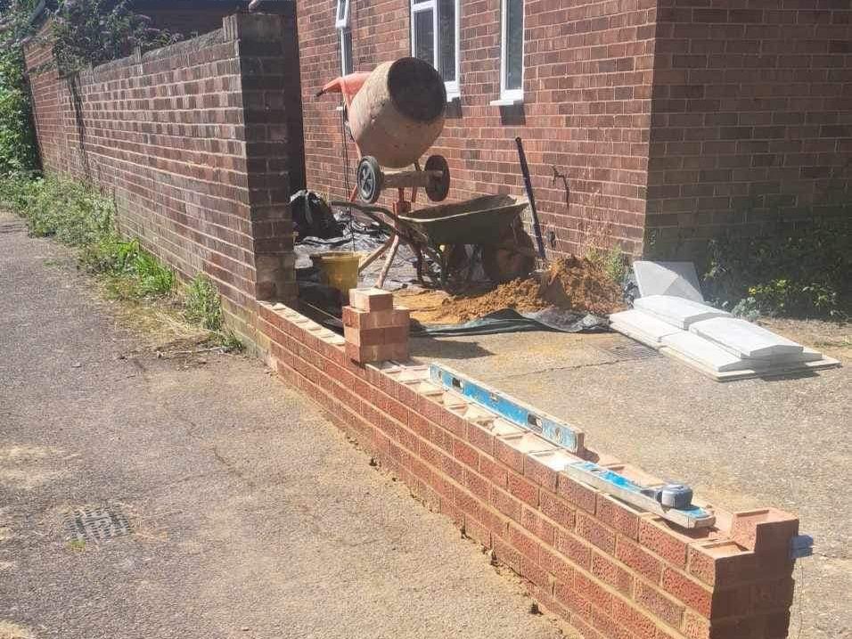 Construction site with a partially built brick wall and a cement mixer nearby.